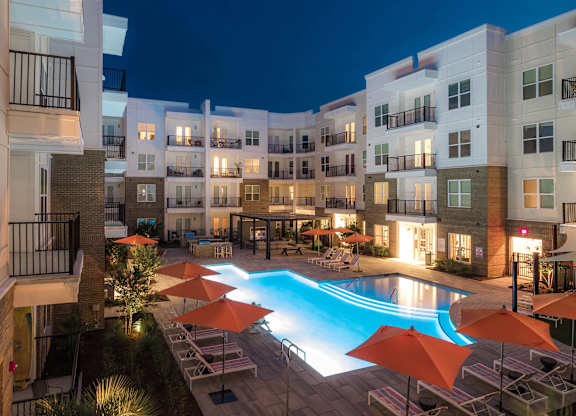 A swimming pool surrounded by orange umbrellas and chairs in a courtyard at night at Hudson at Renaissance Apartments, Wilmington
