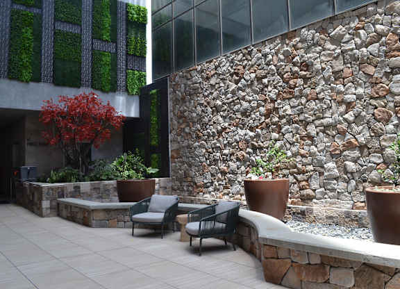 A patio with a stone wall and a green tree.