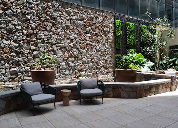 A patio with a stone wall and two chairs.