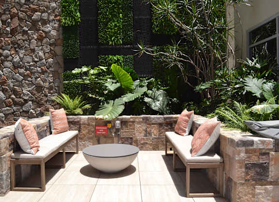 A stone wall with a planter and two chairs with cushions.