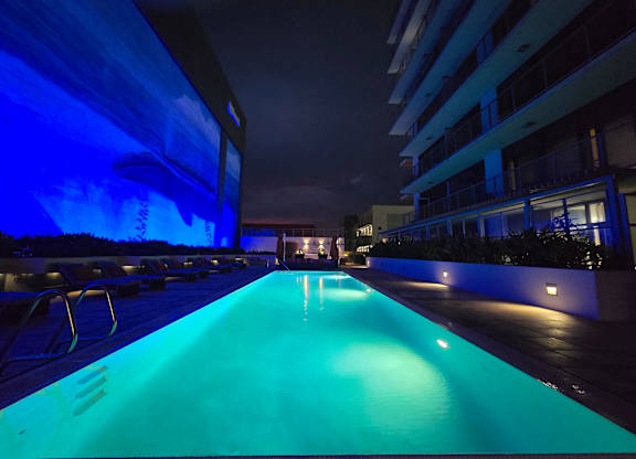 A long rectangular pool lit up with blue lights at night.