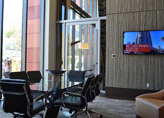 A conference room with a large screen on the wall and chairs around a table.