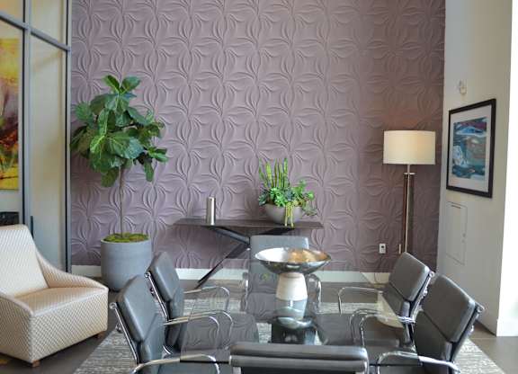 A grey table surrounded by grey chairs in a room with a purple patterned wallpaper.