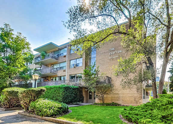 an apartment building with a lawn and trees in front of it