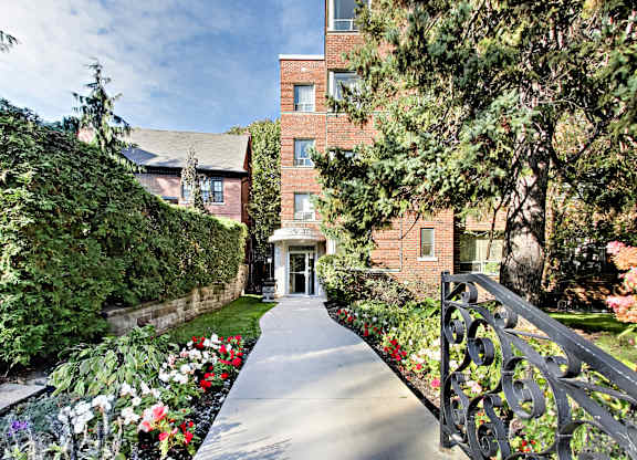 a walkway leading to a brick building with trees and flowers