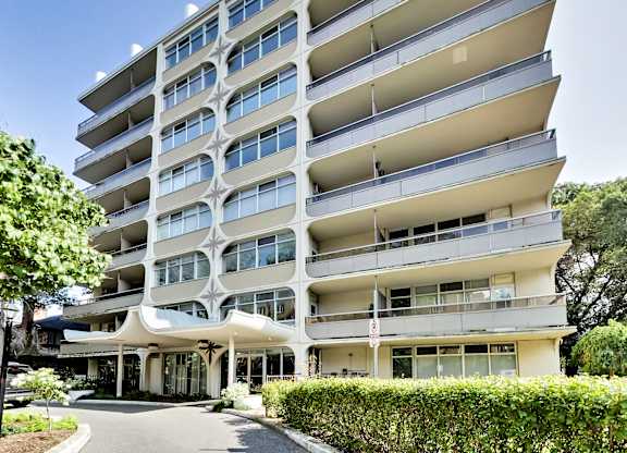 A large white apartment building with balconies and a covered walkway.