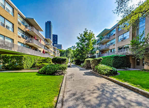 a path between two apartment buildings with green grass and trees