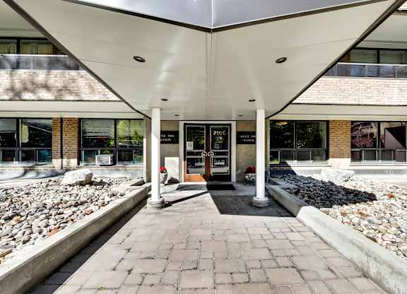 the front entrance of a building with a brick walkway and a rock garden