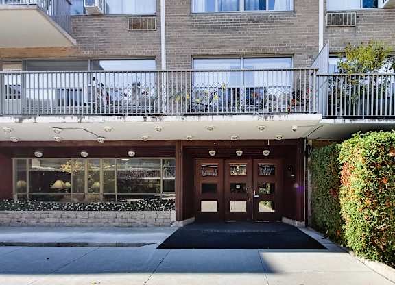 the front door of a building with a sidewalk and a balcony