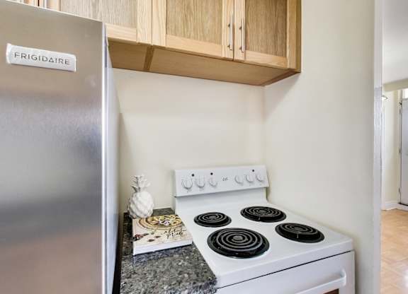 A stainless steel fridge with a white stove in front of wooden cabinets.