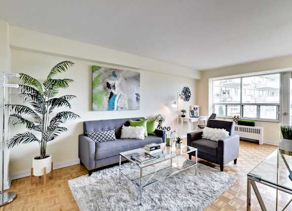 A living room with a grey couch, a glass table, and a large painting on the wall.
