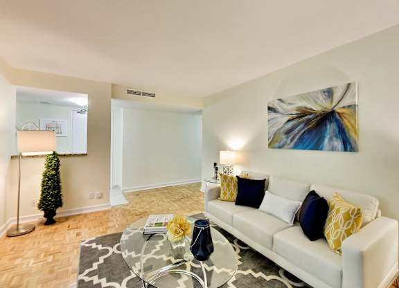 A living room with a white couch and a painting on the wall.