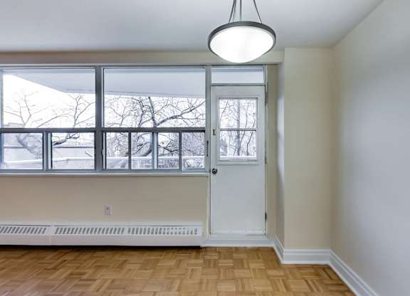 A room with a white door and a window with a view of trees outside.