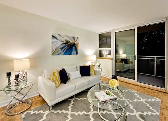 A living room with a white couch, a glass coffee table, and a painting on the wall.