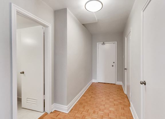 an empty hallway with white walls and wood flooring and a closet