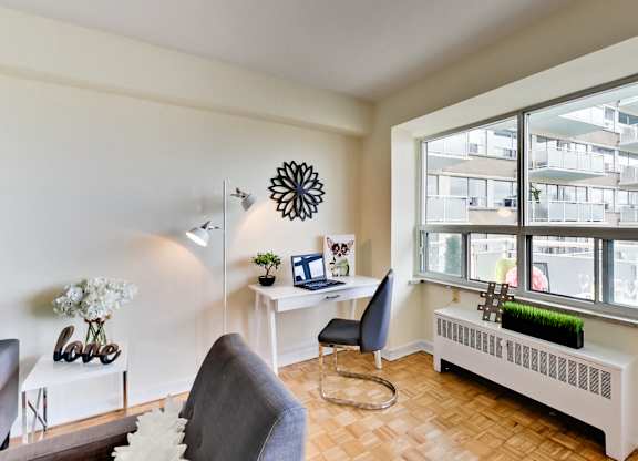 A room with a grey chair and a white desk with a laptop on it.