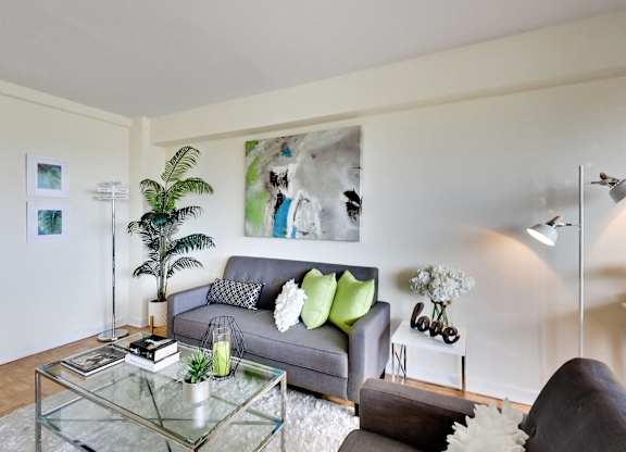 A living room with a grey couch, a glass coffee table, and a large painting on the wall.