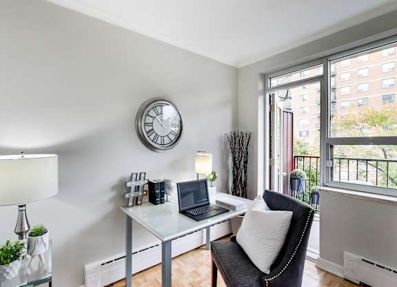 a living room with a desk with a laptop and a clock on the wall