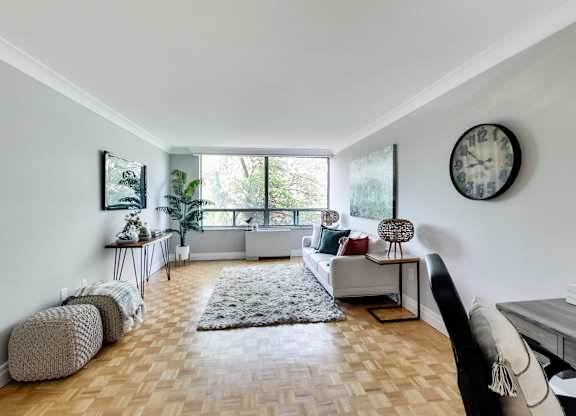 A living room with a white couch, a grey rug, and a clock on the wall.
