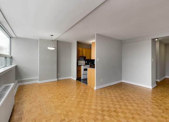 an empty living room with wood flooring and a kitchen