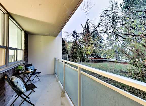 A balcony with chairs and a table overlooking a backyard.