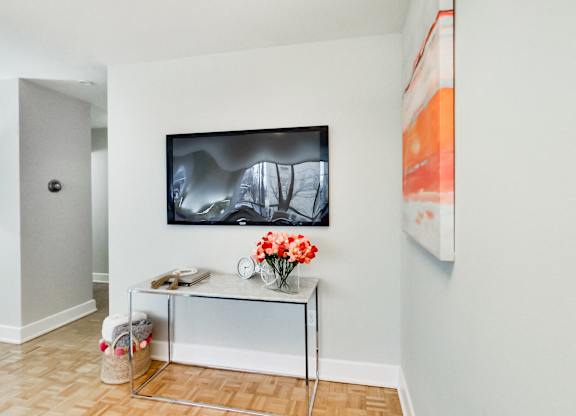 A modern living room with a flat screen TV mounted on the wall above a console table with a vase of flowers on it.