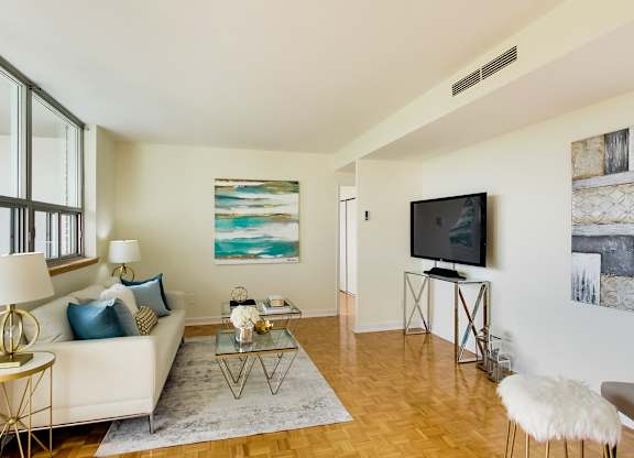 A living room with a white couch, a glass coffee table, and a television.