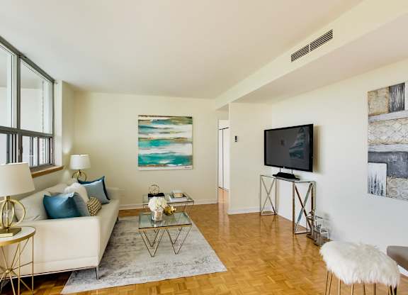A living room with a white couch, a glass coffee table, and a television.