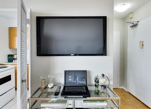 A black laptop is on a glass coffee table with a remote control and a book titled