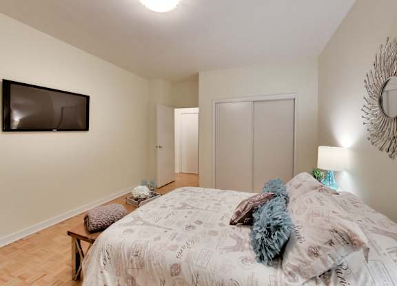 A bedroom with a bed, a bench, a mirror and a television.