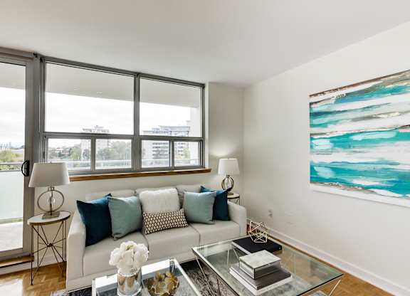 A living room with a white couch, a glass coffee table, and a large painting on the wall.