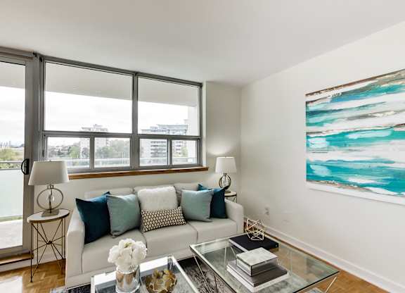 A living room with a white couch, a glass coffee table, and a large painting on the wall.