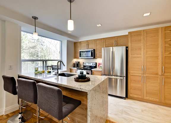 a kitchen with wooden cabinets and a marble counter top and a stainless steel refrigerator