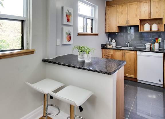 A kitchen with a black countertop and white stools.