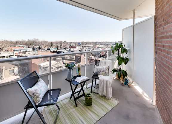 A balcony with a chair, table, and potted plant overlooking a cityscape.
