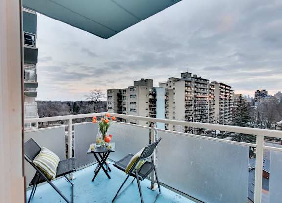 A balcony with a table and chairs overlooking a cityscape.