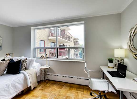 a bedroom with a large window and a bed and a desk with a laptop