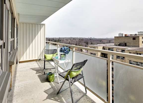 A balcony with a table and chairs overlooking a cityscape.