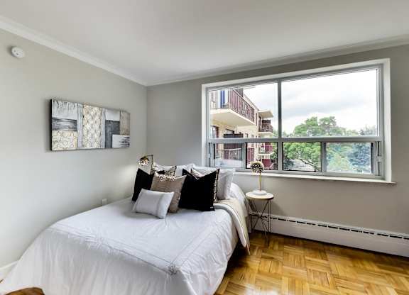 a bedroom with a large window and a bed with white sheets and pillows