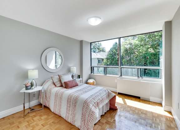 A bedroom with a bed, nightstand, and a round mirror on the wall.