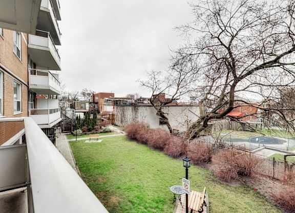 A balcony overlooks a green yard with a tree and a building in the background.