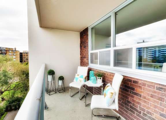 A balcony with a white chair and a small table with a plant on it.