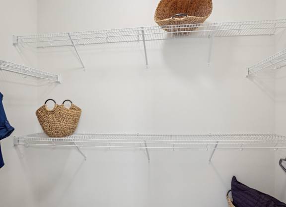 A white wall with three shelves and a basket on the top shelf.