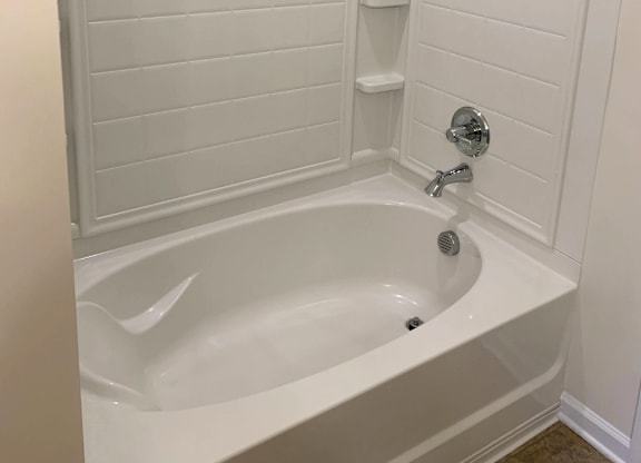 A white bathroom with a white tub and a white shower head.