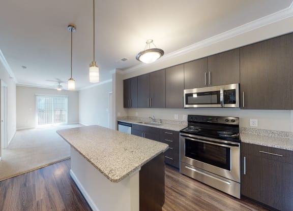 Kitchen with island, dark cabinets, vinyl floors and granite countertops; open to living room
