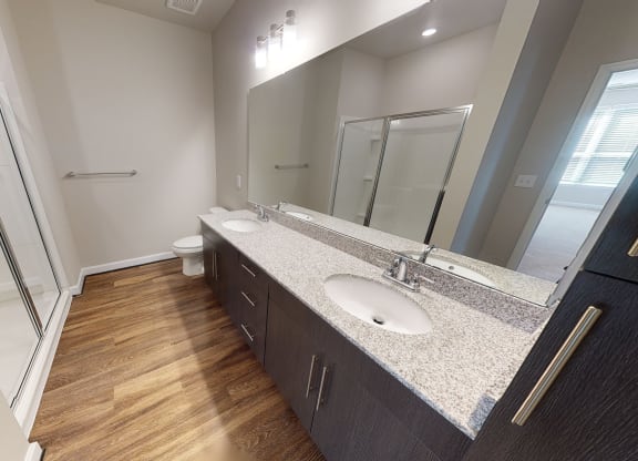 Bathroom with dual sinks, dark cabinets, toilet and walk-in shower