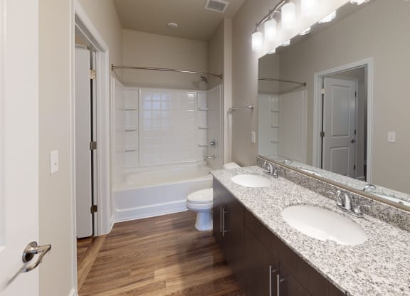 Bathroom with dual sinks, dark cabinets, toilet and shower with bathtub