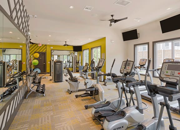 Luxury Apartments in Charlotte, North Carolina with In-Unit Washer and Dryer - Belmont at Tryon - Fitness Center With Cardio Machines, Strength Equipment, Large Mirrors, Ceiling Fans, And Windows.