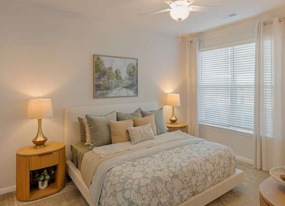 A bedroom with a large bed, two lamps, and a painting on the wall.