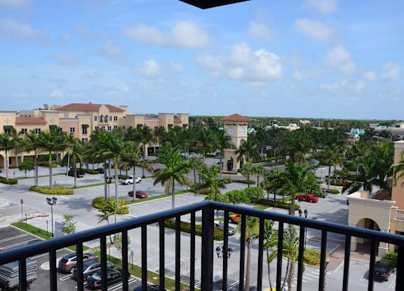 A view from a balcony overlooking a parking lot surrounded by palm trees.